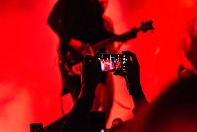 前面的人拿着智能手机一个人弹吉他在舞台上

